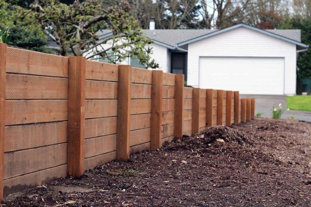 A wooden fence stands in front of a house framing the property and enhancing its rustic charm