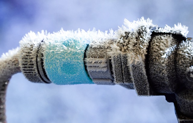 Frost-covered outdoor faucet with intricate ice crystals forming on the metal and blue hose connector.