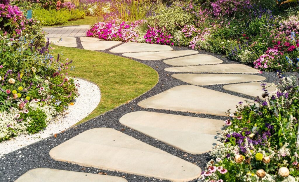 A stone pathway winds through a garden filled with colorful flowers and lush green grass