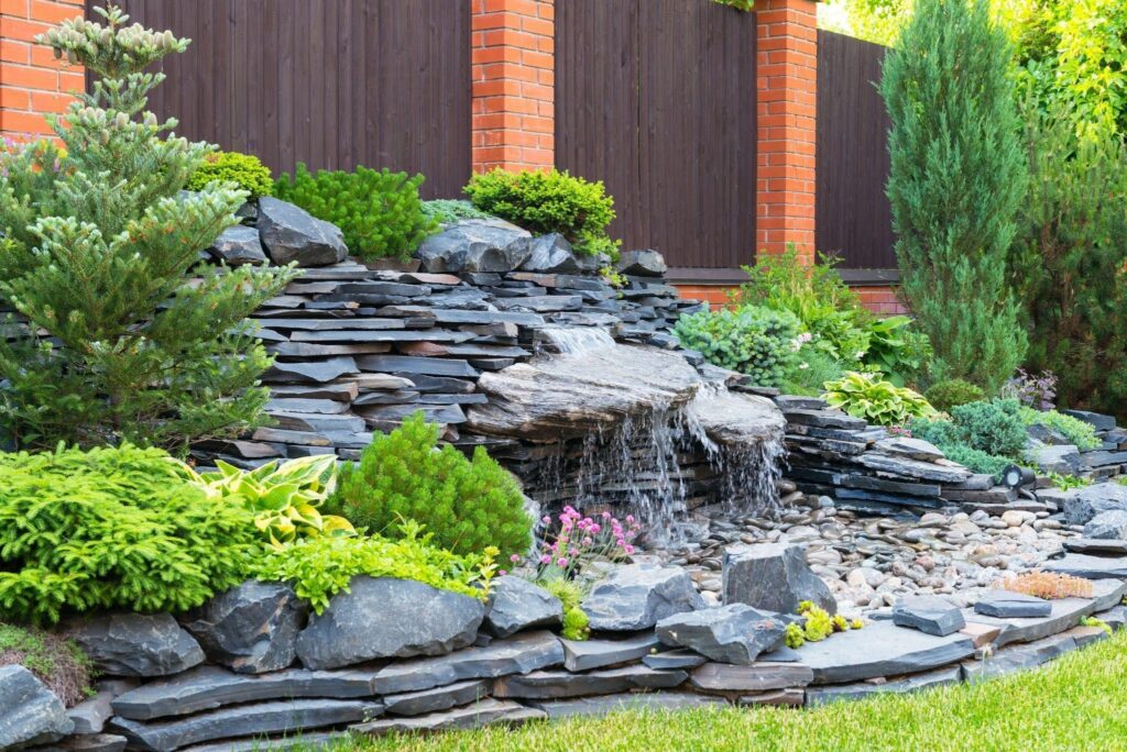 A serene garden featuring a cascading waterfall surrounded by lush greenery and smooth rocks