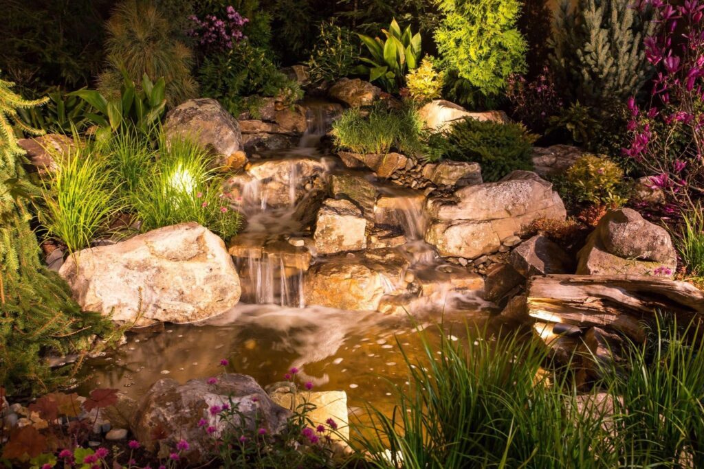 A serene waterfall cascades in a garden illuminated by soft lights under a starry night sky